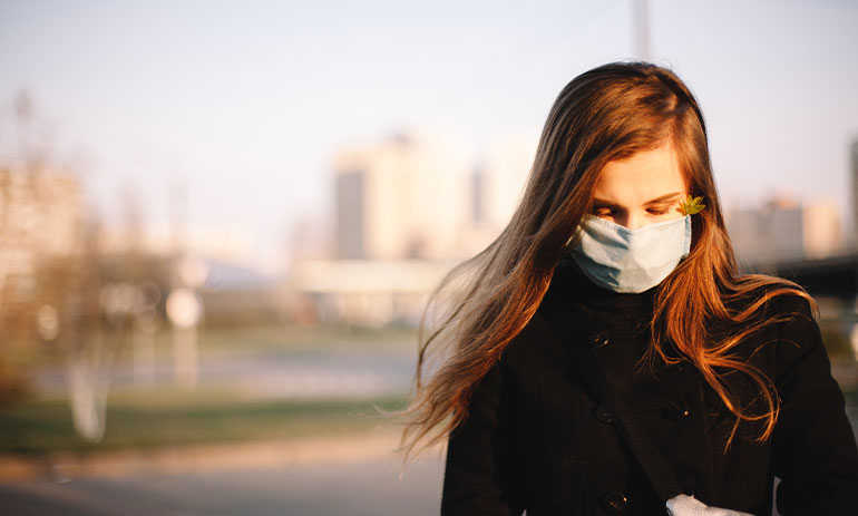sad teenage girl wearing protective face medical mask standing outdoors on city street