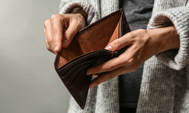 Woman showing her empty purse on grey background