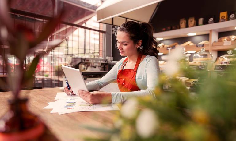 woman in a cafe wearing red apron sat at table doing paperwork