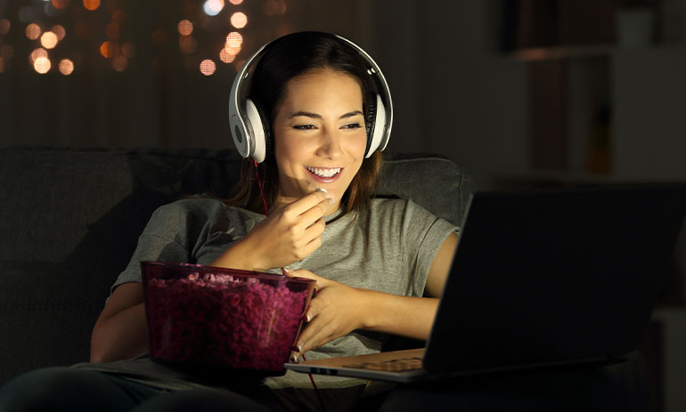 woman watching something on her laptop eating popcorn