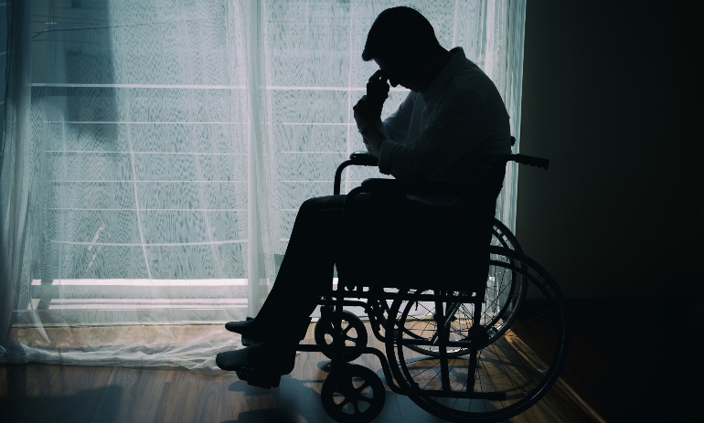 Silhouette of handicapped Man sitting on wheelchair in front of a large panoramic window in hospital,He is sad and lonely.