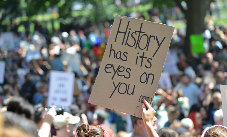 protester holding a sign that says history has its eyes on you