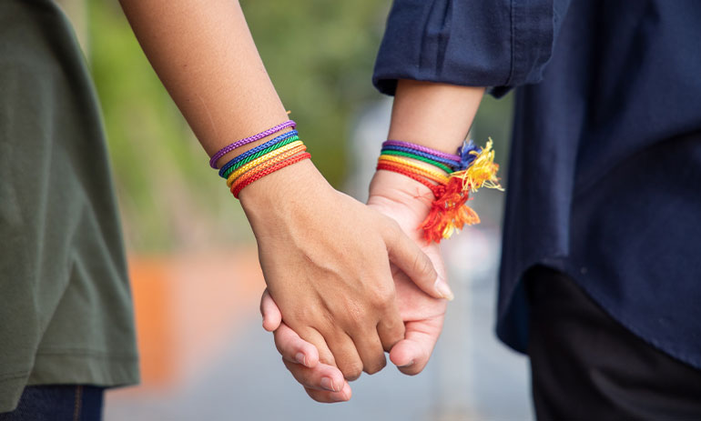 close up of couple holding hands wearing rainbow bracelets