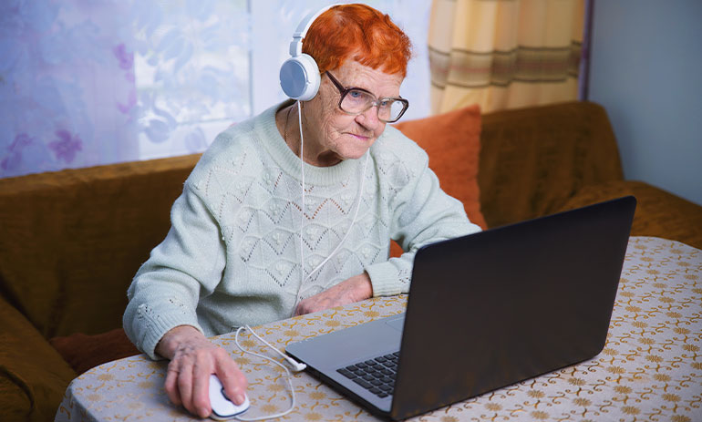 an older woman learning to use a computer - sat at a laptop on her table.