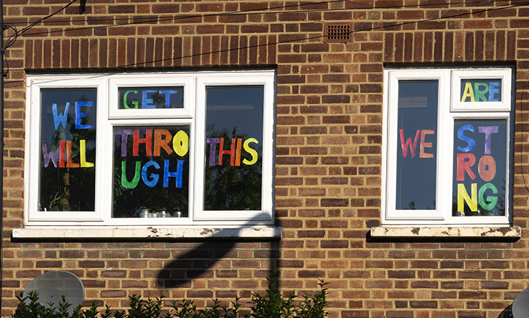 brick building with signs in the window saying "we will get through this, we're strong"