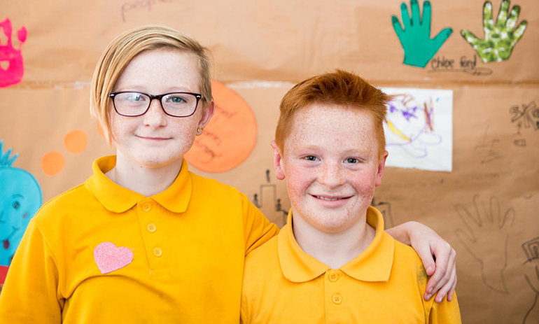 Two children standing next to each other smiling wearing yellow tshirts