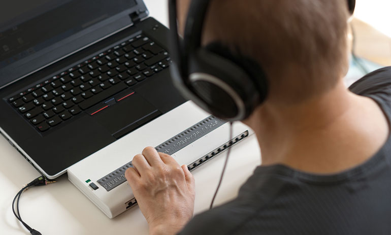 Blind person working on computer with braille display and screen