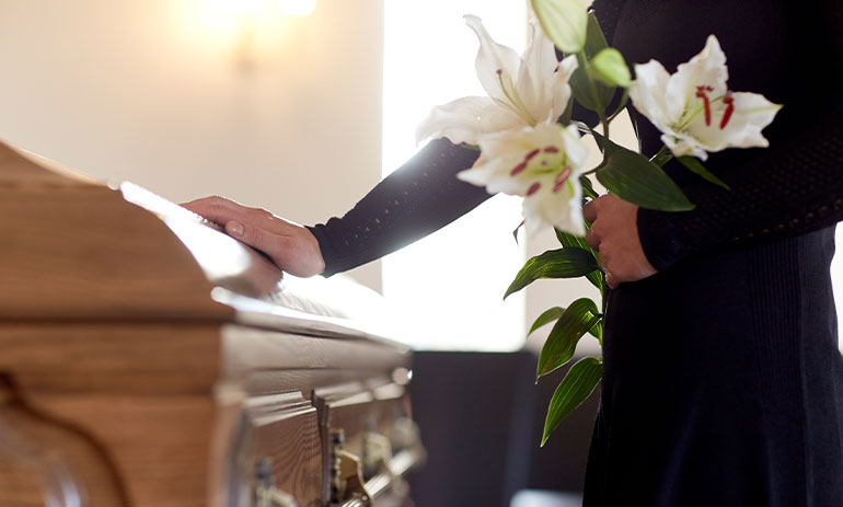 Person at a funeral holding flowers with one hand on a coffin