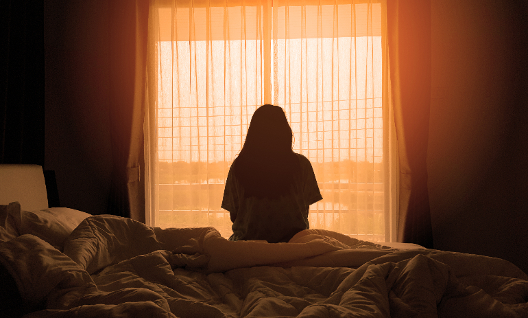 Woman looking out window while sitting on bed