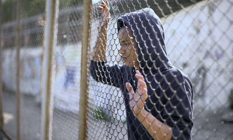 teen looking through a wire fence