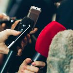 close up image of journalists holding microphone up to record someone speaking