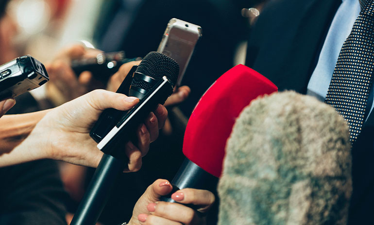 close up image of journalists holding microphone up to record someone speaking