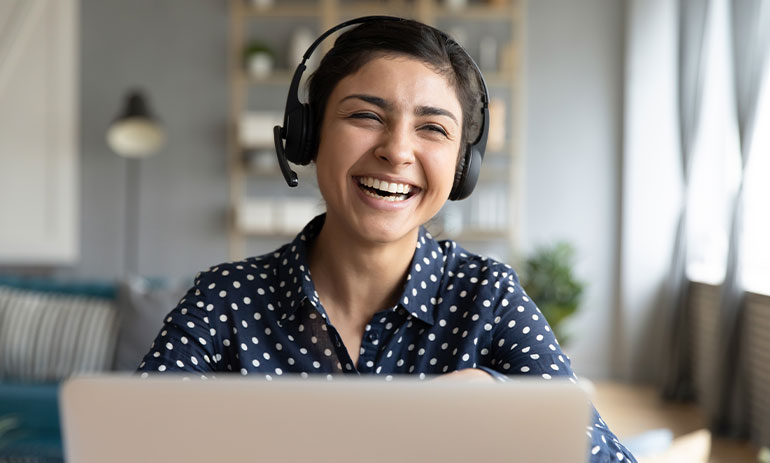 smiling woman wearing headphones looking at her laptop