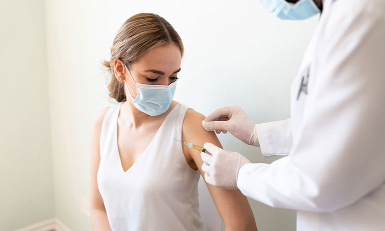white woman in white t-shirt wearing face mask getting a vaccine