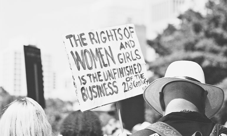 Person holding sign "The rights of women and girls is the unfinished business of the 21st century"