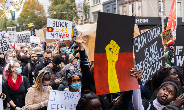 Black Lives Matter protest in Melbourne. Sign in the foreground in the colours of the Aboriginal flag with a raised fist