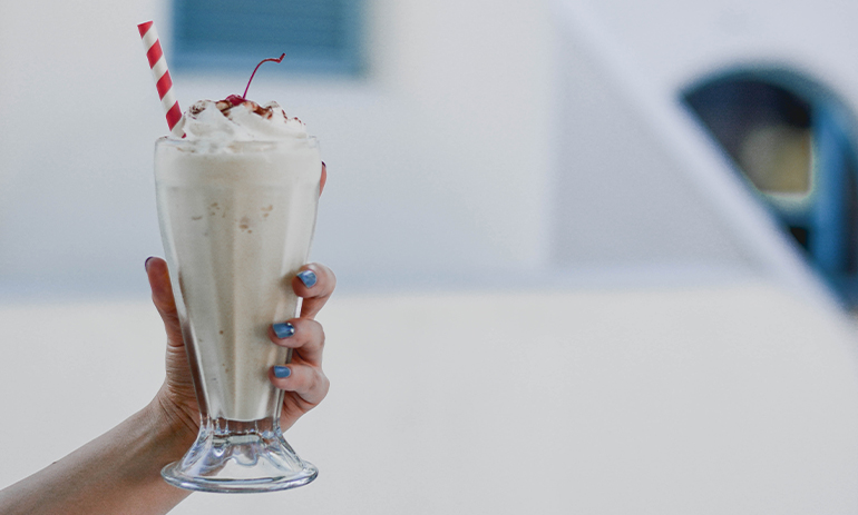handing holding a glass of milkshake with cream and a cherry on top with a straw