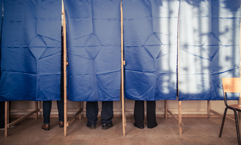 polling booth, three sets of feet visible behind blue curtain