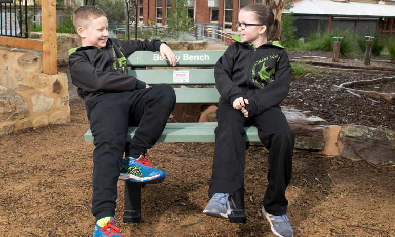 Hunter and Chloe sit on an outdoor bench made from recycled plastic