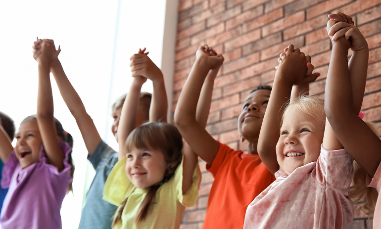 line of smiling children with their arms in the air holding hands