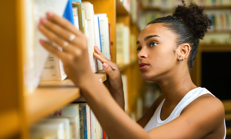 a young woman taking a book off a shelf in a library