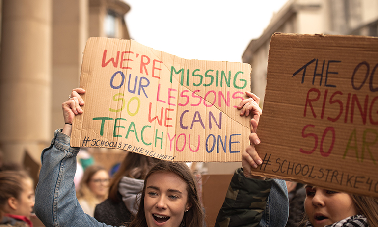 young girl holding up a sign saying "we're missing our lessons so we can teach you one" at a climate strike.