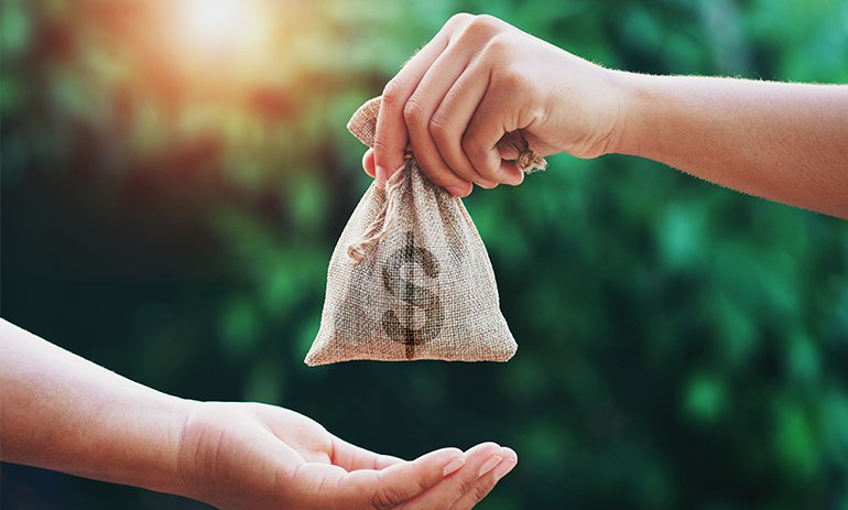 A close up of a hand holding a cloth bag with a dollar sign on it