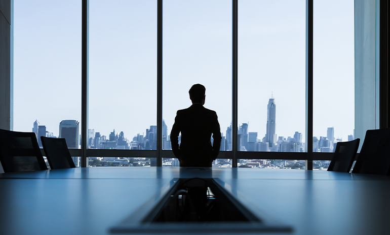 silhouette of a man standing in a boardroom looking out a window with a city skyline