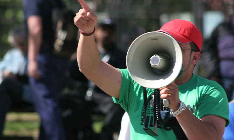 protester wearing a green t-shirt shouting into a megaphone