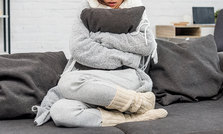 cold woman wrapped up in jumpers and scarf on a sofa