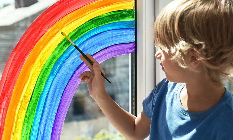 young boy painting a rainbow on his window