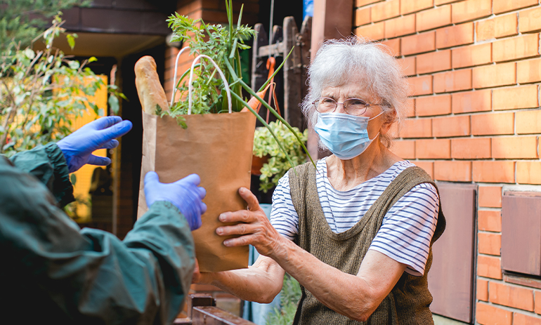 elderly woman wearing a facemask receiving a bag of food