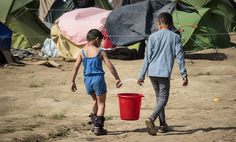 two boys carrying a bucket between them in a refugee camp