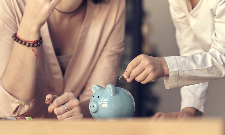 close up on two people, one is putting a coin in a blue piggy bank
