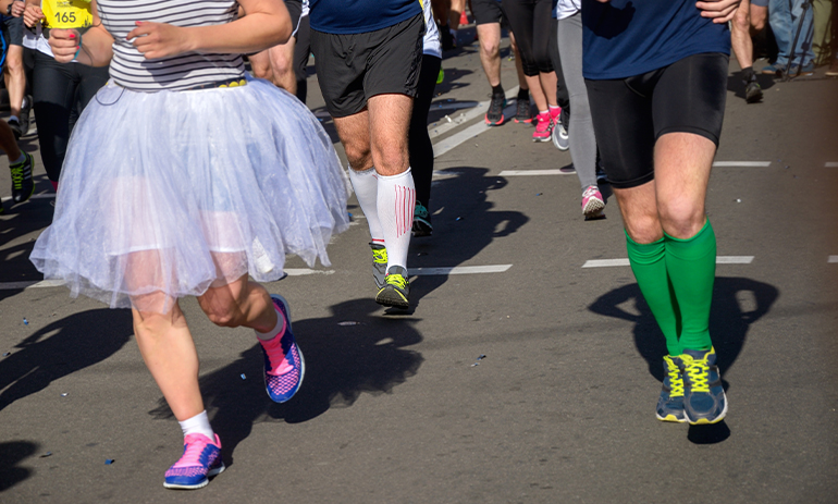 legs of people running in a fun run, the person at the front is wearing a tutu