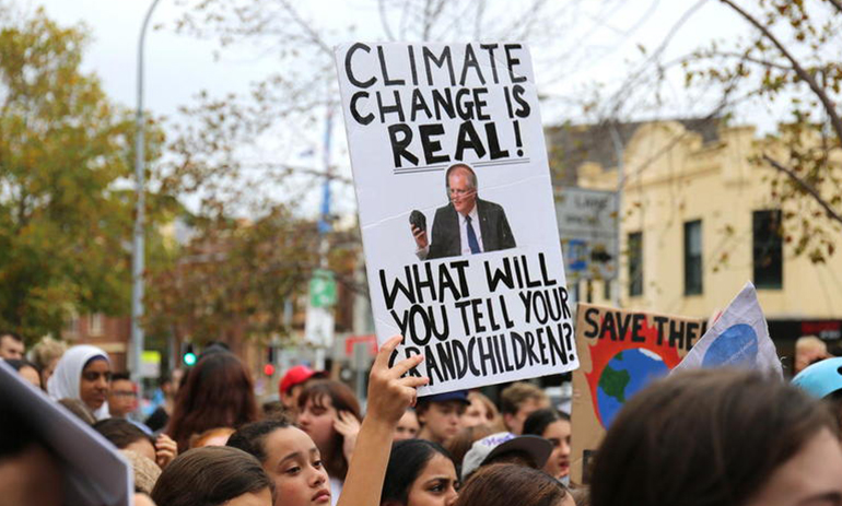 student at the School Strike for Climate in Sydney holding a banner with an image of Scott Morrison holding a piece of coal with the words climate change is real