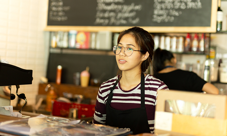 Young Asian woman with glasses at work wearing apron standing in coffee shop