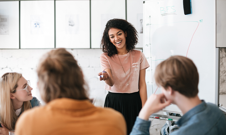 woman with dark hair presenting on whiteboard to three colleagues