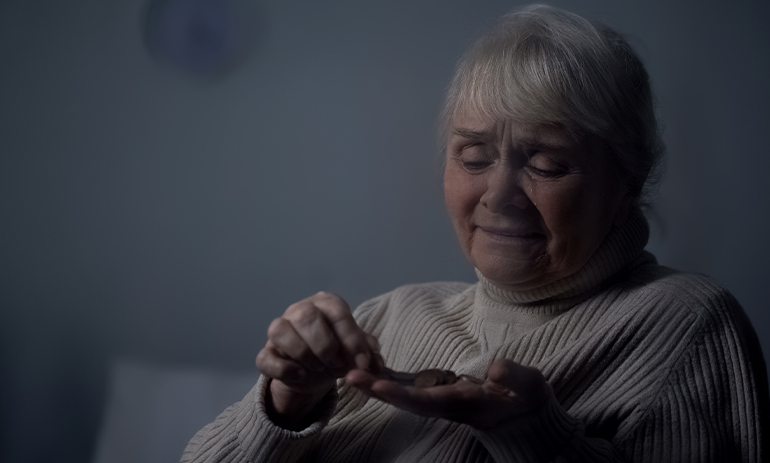 older woman sitting in dark looking at coins in her hand