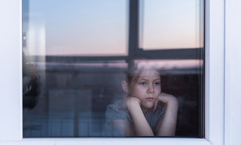 A sad, lonely child sits on the windowsill and looks out the window