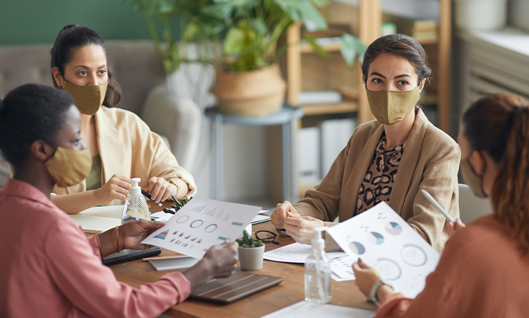 High angle view at multi-ethnic group of young businesswomen wearing masks during meeting in office