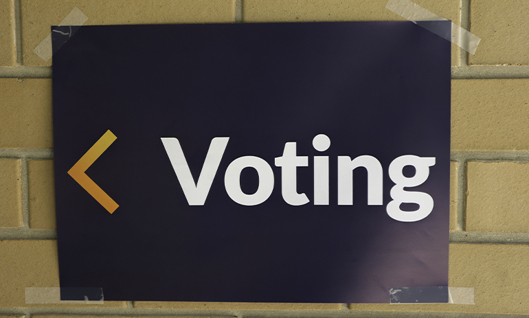 White text on blue background voting sign on brickwork with arrow