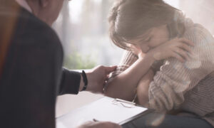 man holding a clipboard comforting an upset woman sitting opposite him