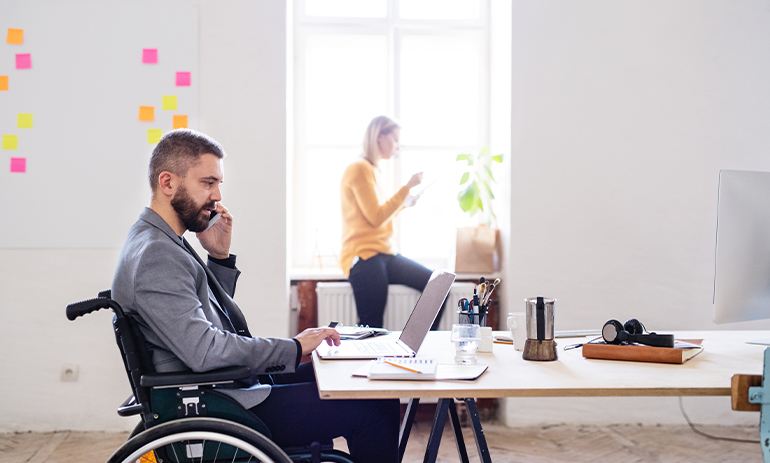 A man in a wheelchair sits in an office talking on the phone