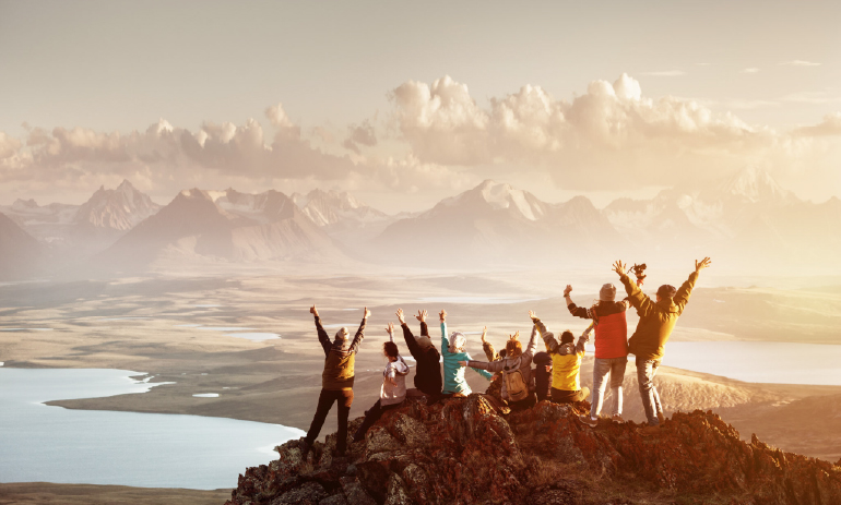 group of people standing on top of a mountain with their hands in the air
