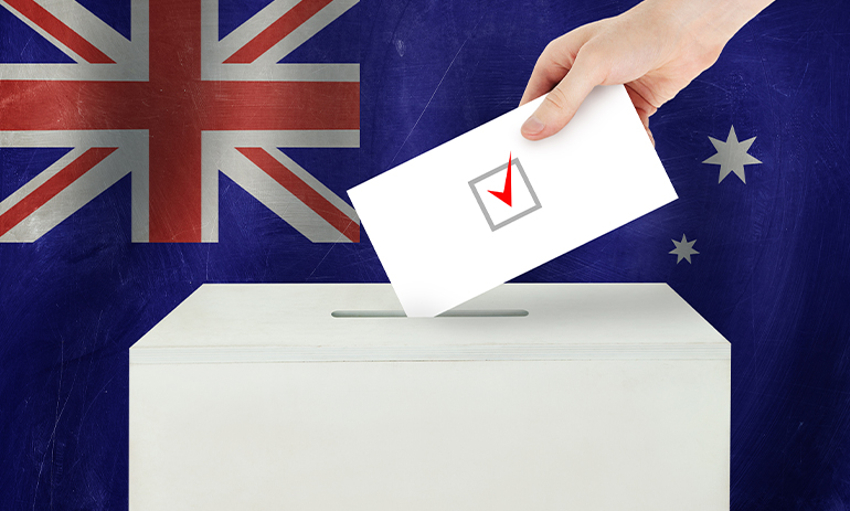 person putting an envelope into a ballot box in front of an Australian flag