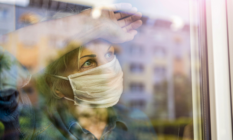 woman with face mask leaning against a window