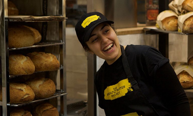 A woman baker stands in front of an oven full of bread