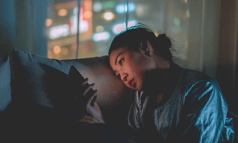 photo of a woman sitting on a sofa in the dark looking at her phone