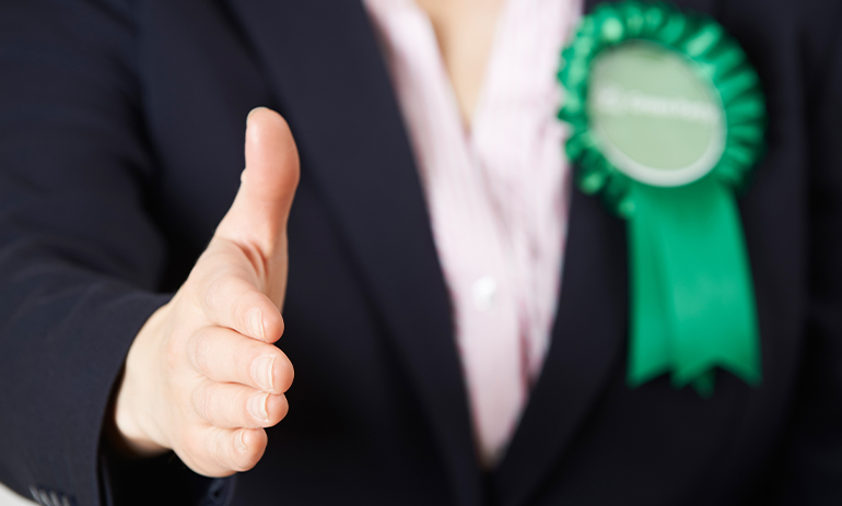 close up person wearing green political rosette holding out hand